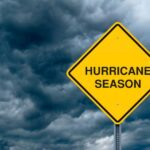 A photograph of a hazard sign that reads "Hurricane Season" with storm clouds in the background.