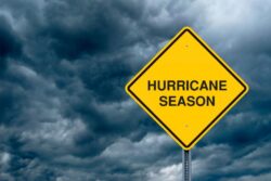 A photograph of a hazard sign that reads "Hurricane Season" with storm clouds in the background.